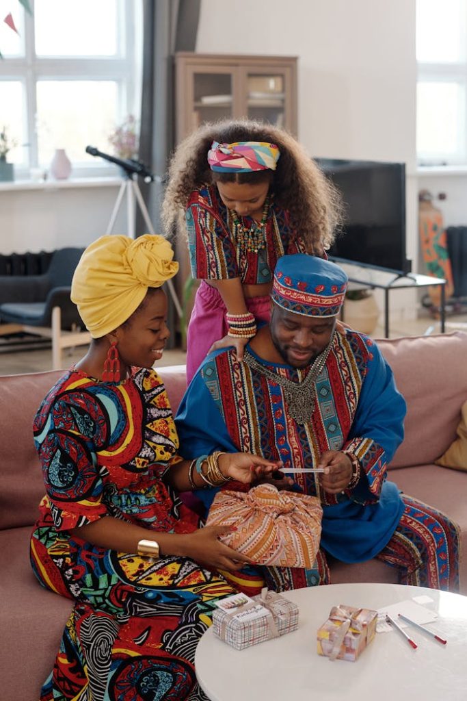 pexels photo 6190857 Joyful family exchanging Kwanzaa gifts in traditional attire, celebrating culture and unity indoors.