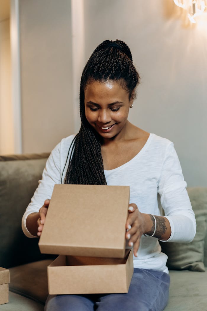 A woman joyously unpacks an online shopping delivery box in a cozy home setting, expressing excitement.