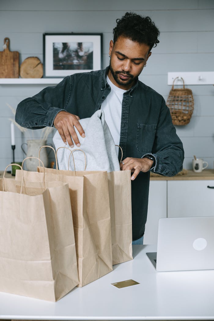 Stress‑Free School Support for Your Children Back Home Adult man organizing purchases with paper bags and laptop in a modern home setting.